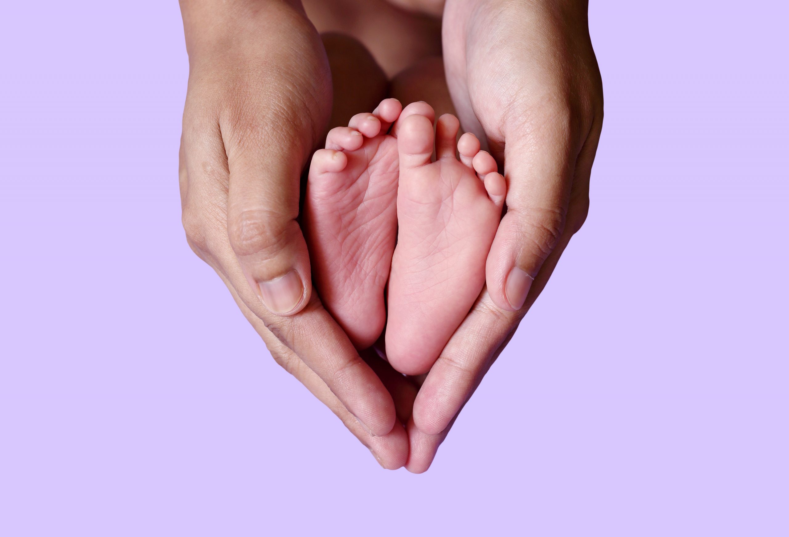 Close up of tiny feet of newborn baby held by adult hands