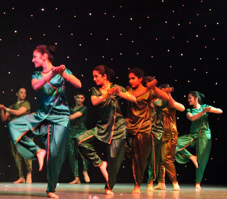 Ramayana performers in green outfits, standing on one leg with the heads facing away from their hands pouring out to the opposite side