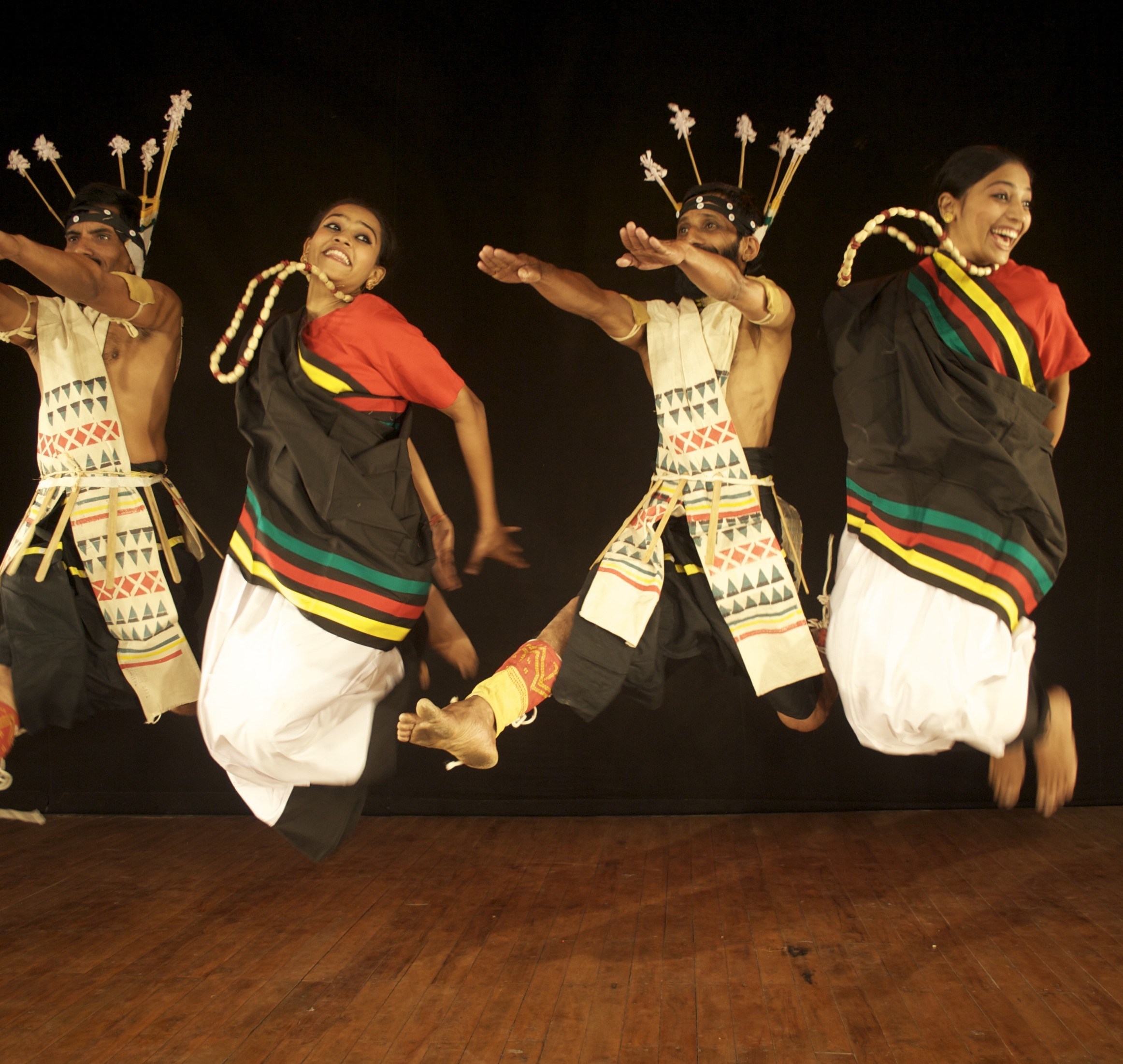 Janavak Folk Dances of India group in red, green, black and yellow outfits mid-jump