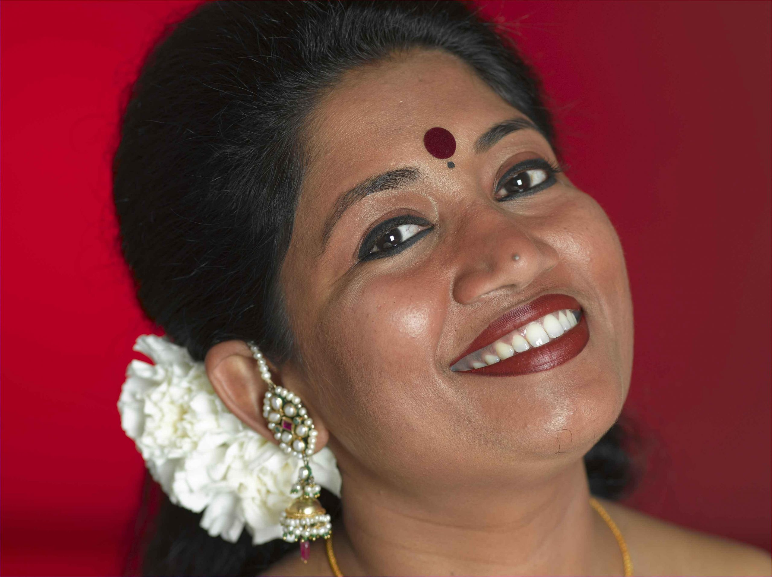 Sanchita headshot against red background with white flowers in her hair