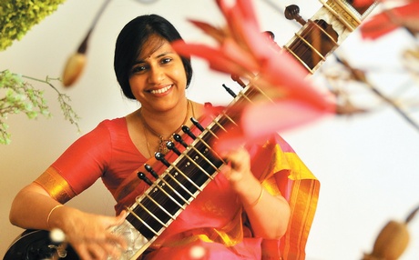 Anupama Bhagwat in a red sari with flowers out of focus with a sitar