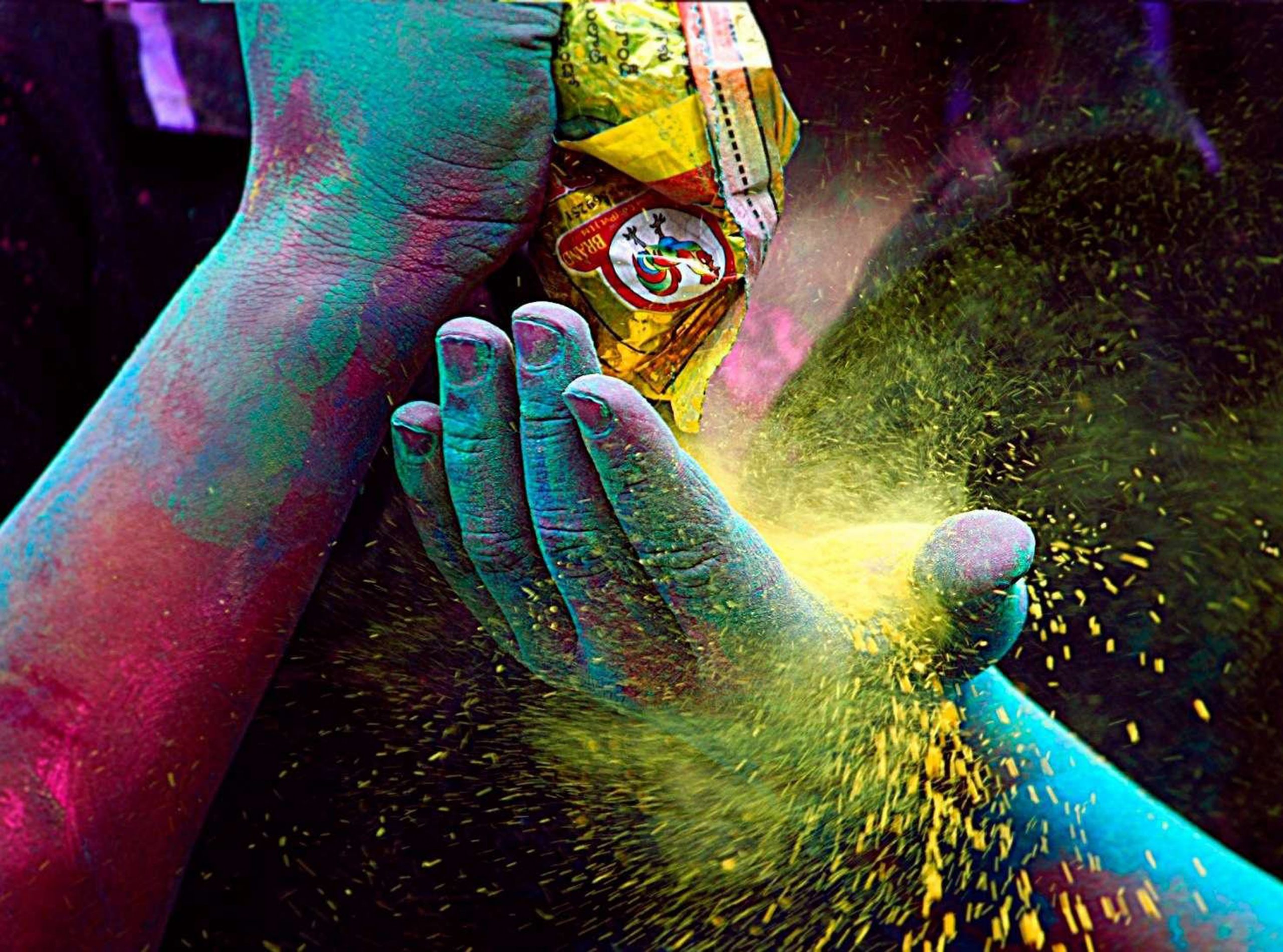 close up on two hands covered in multi-coloured Holi powder pour yellow powder into the other hand