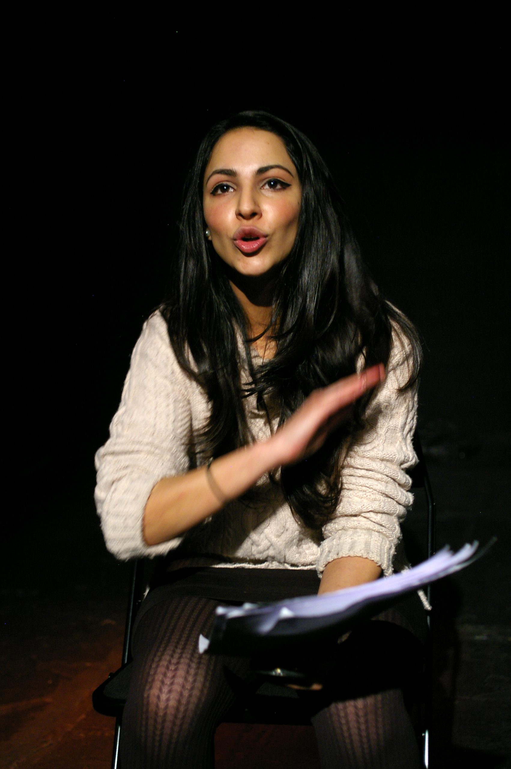 professional performance photo of a girl sat holding script speaking with a hand moving across her chest