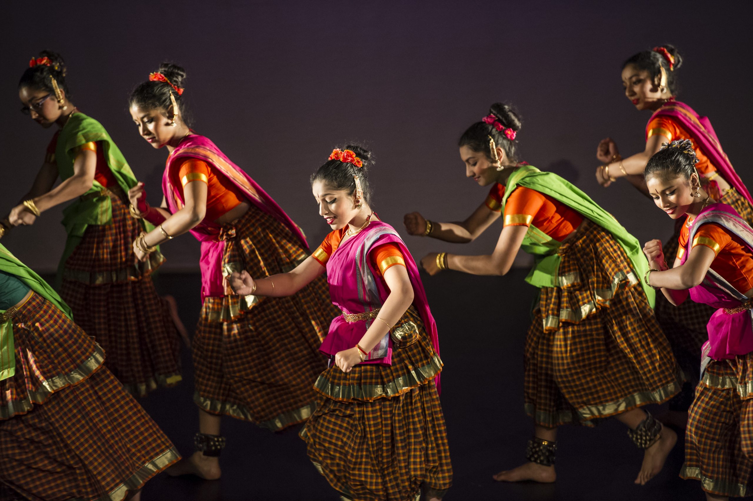 A group of girls in pink, orange and green outfits mid Bharatnatyam performance