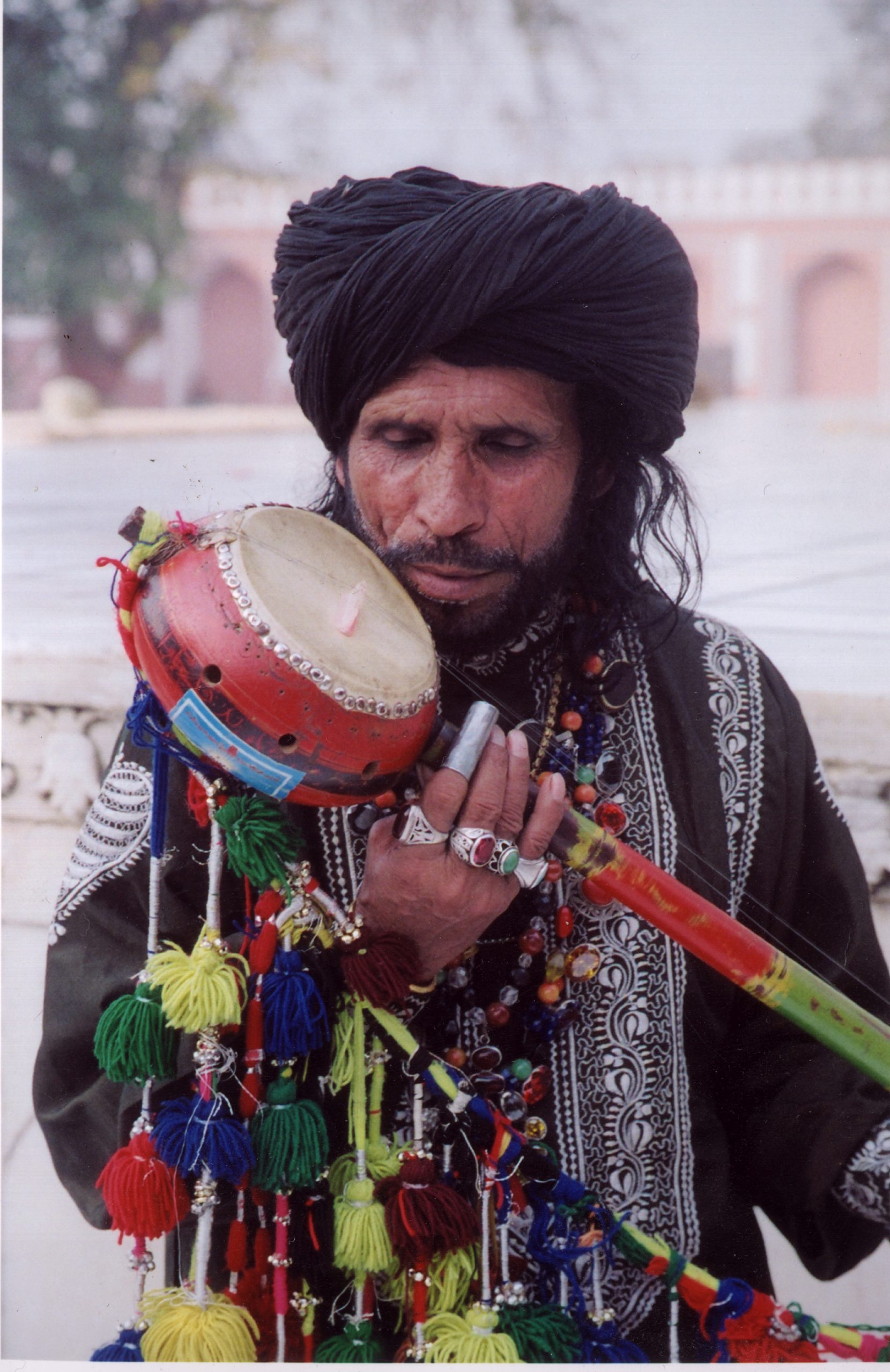 Sain Zahoor in a black and white outfit holding a colourfully decorated and held instrument