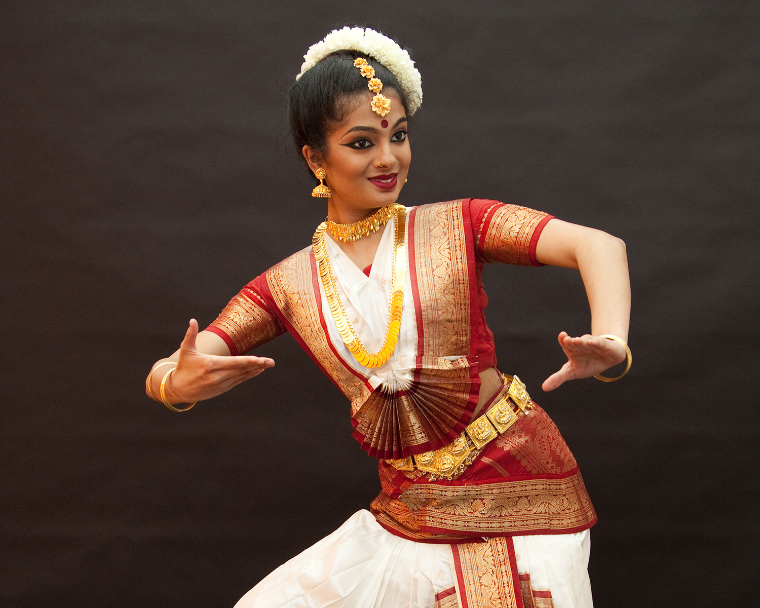 Anaya Bolar Mohiniattam in a red and white Classical Indian dance outfit holding a pose with her hands in front of her