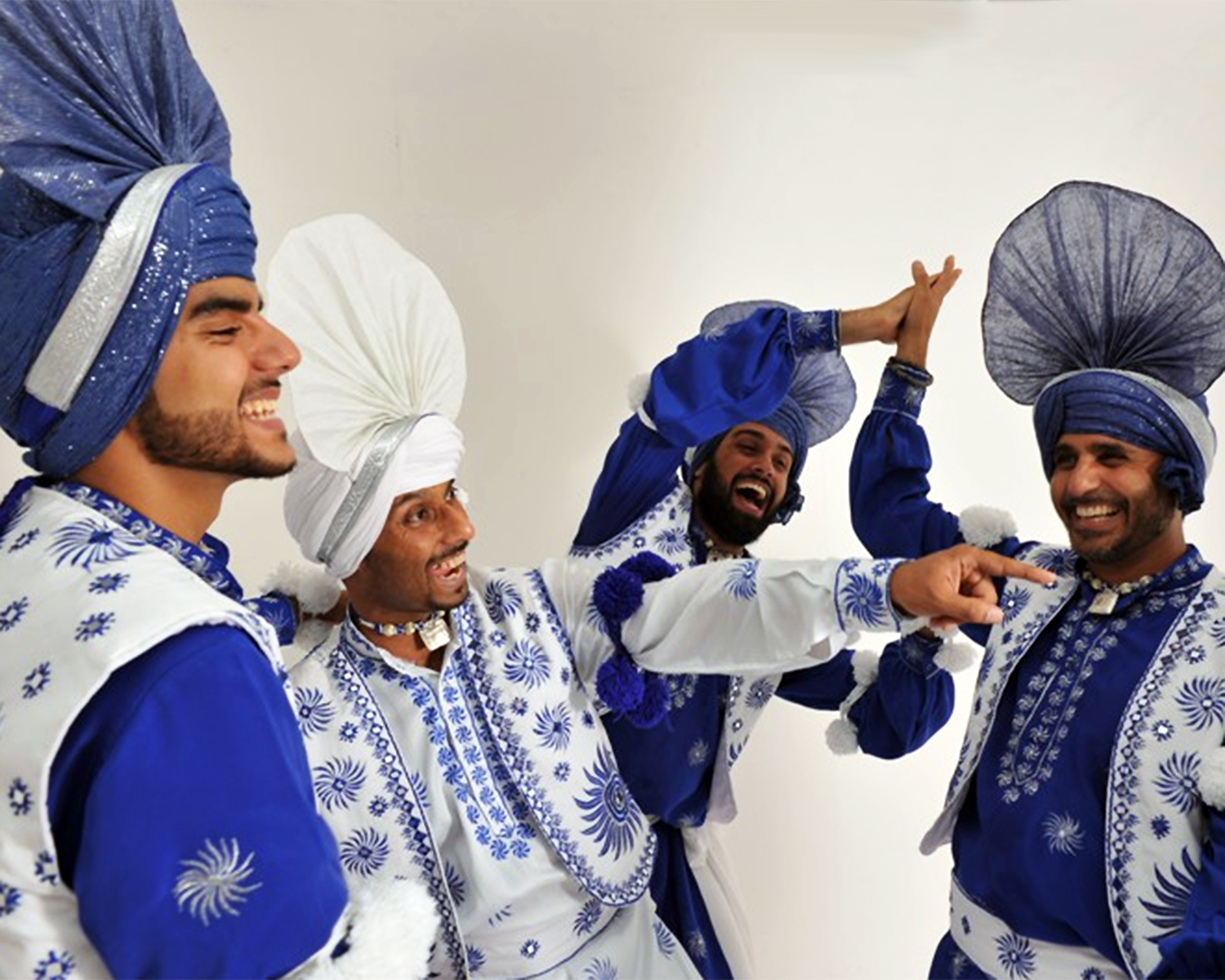 men in blue and white traditional outfits with turbans, kurtas and waistcoats laughing and high fiving