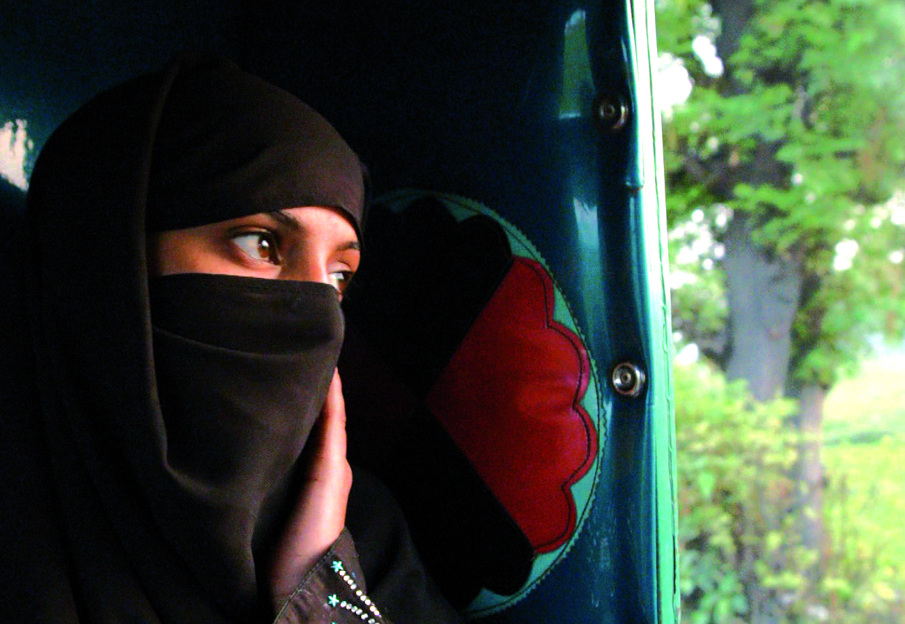 A woman in a burkha holding her cheek looking out of a teal and red carriage