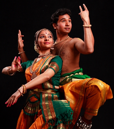 a male and female dancer posing looking to the right, both dressed om green and orange holding Indian classical dance pose next to each other
