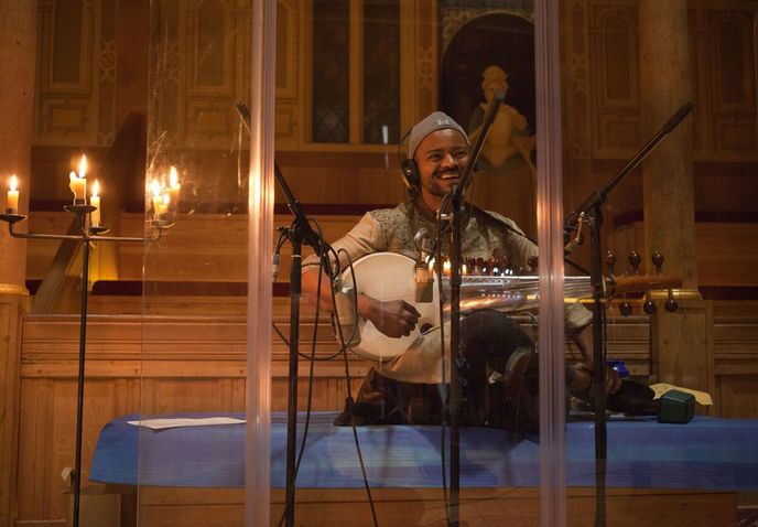Soumik Datta with a stringed instrument hooked up to microphones in a candle-lit studio