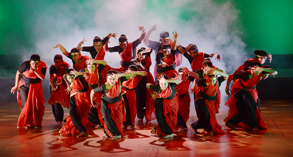 a group of dancers in red and black in a tight formation all with their hands pressing outwards with stern, beady eyed faces