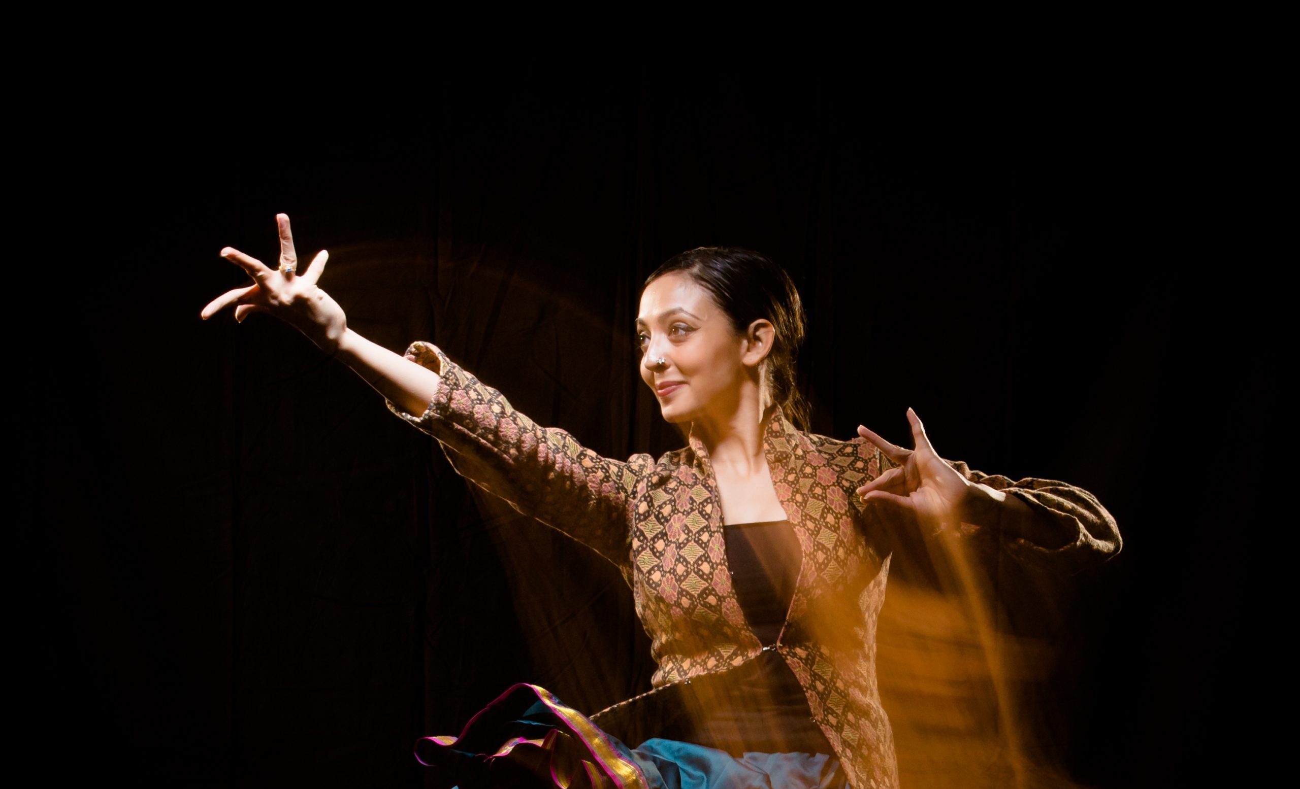 Gandini Juggling in a colourful patterned kurta in a professionally shot action photo mid-dance move with one arm close to her and the other extended