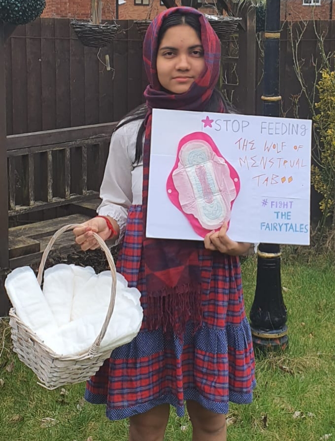 a young girl with a basket of sanitary towels holding up a poster reading 'fight the fairytales'