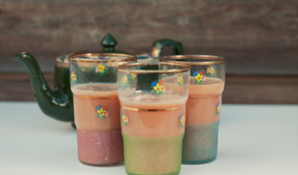 Three chai glasses in multicoloured glasses with a teapot in the background
