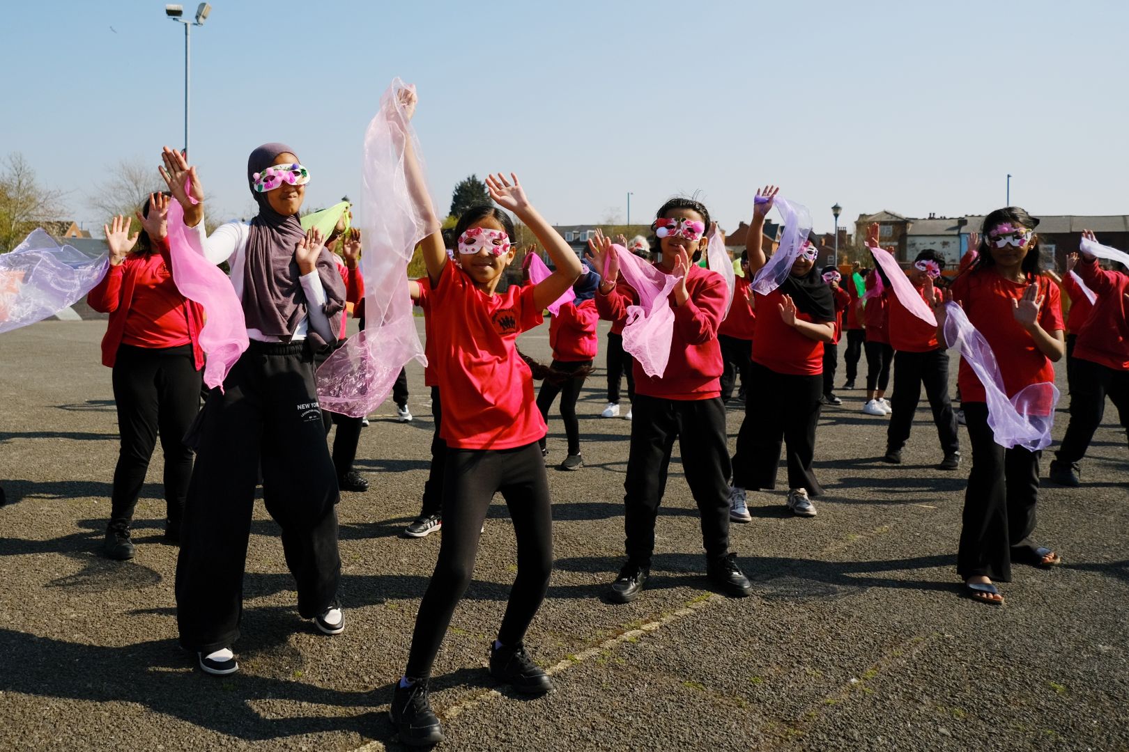 group of children in hand decorated masks and pink scarves dancing