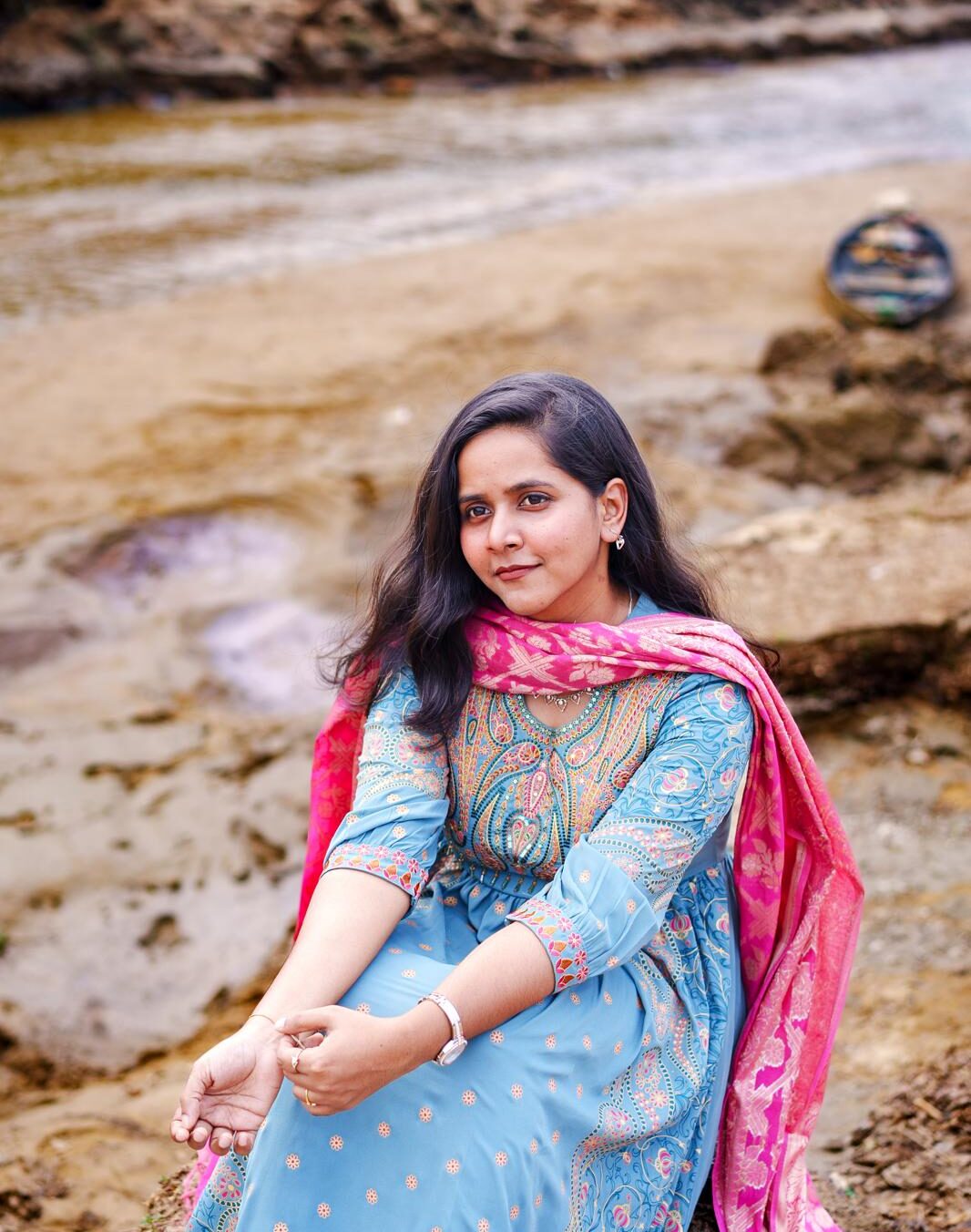 A female in blue and pink Indian outfit posing, looking off in a natural environment