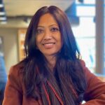 Sonali Dutta. Head and shoulders looking at camera wearing a brown coat