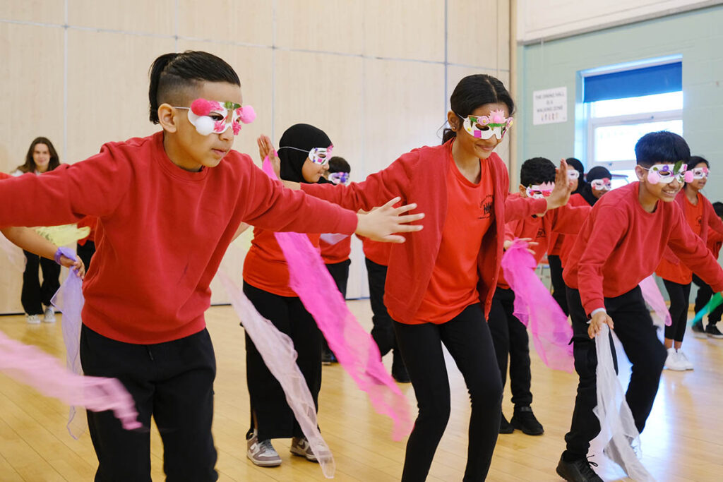 Children dressed in red school uniform wearing eye masks and using scarves in a dance workshop