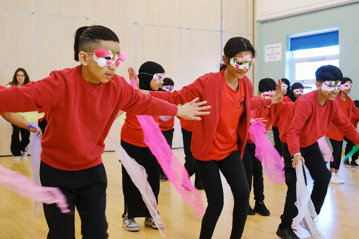 Children dressed in red school uniform wearing eye masks and using scarves in a dance workshop
