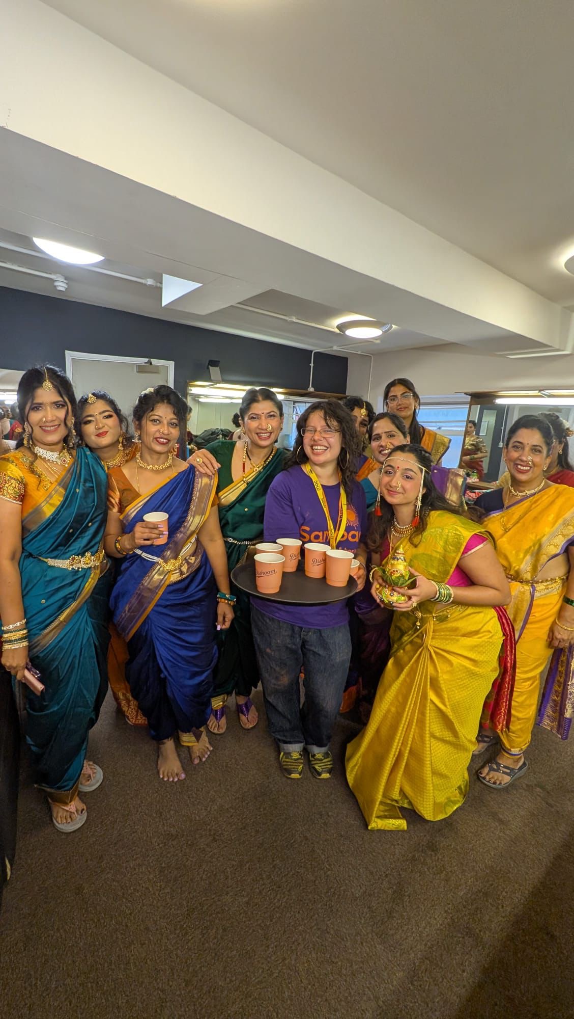 Samapd team member, Mia Goldberg wearinga Sampad logo tshirt with a group of female Indian Dancers in traditional dress